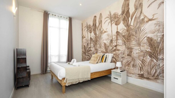 Une chambre à coucher comprenant un lit, une table de chevet, une étagère fixée au mur et une grande fenêtre avec des rideaux.