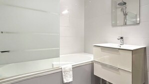 Une salle de bain moderne avec une douche à parois de verre, une baignoire sur pieds, un meuble-lavabo avec miroir et un carrelage foncé.