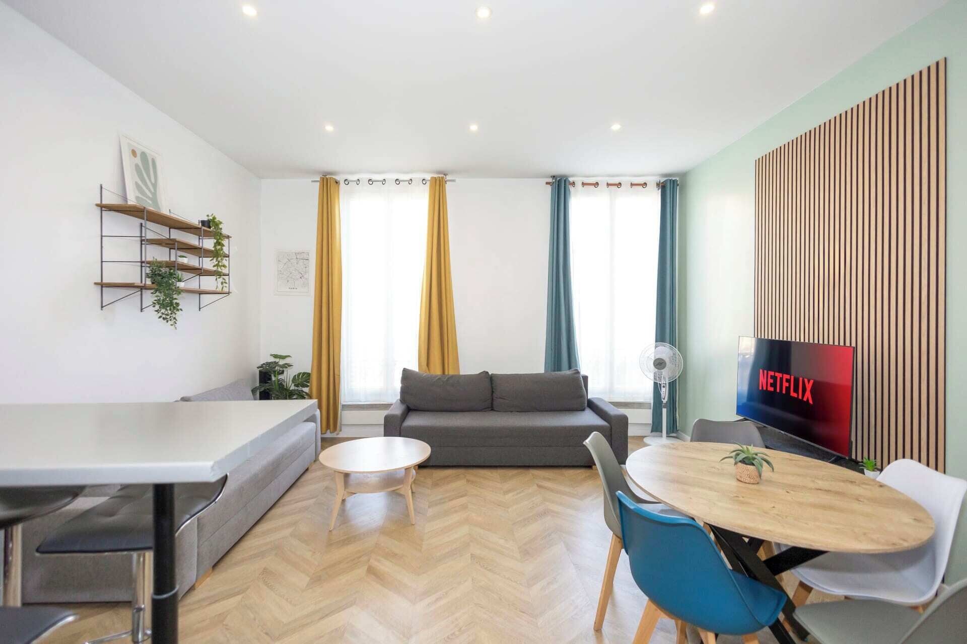 Een moderne woonkamer met een bank, een eettafel met stoelen, een televisie en een wandplank met planten.