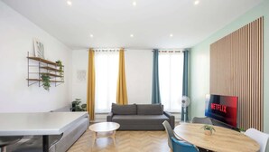 Un salon moderne comprenant un canapé, une table à manger avec des chaises, un téléviseur et une étagère murale agrémentée de plantes.
