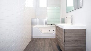 A modern bathroom with a white bathtub, a vanity with a mirror, and a window. - Daumesnil Grand - Two Bedroom Apartment, Sleeps 6 (Paris)
