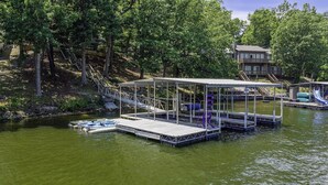 A lakeside dock with a covered seating area, a boat ramp, and a house in the background. - Making Lake Memories, Water Toys, Launch area /Dock/Slip, Fire pit, parking for group. (Linn Creek)