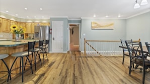 A spacious kitchen with wooden cabinets, a central island with bar stools, and a dining area with a railing. - Making Lake Memories, Water Toys, Launch area /Dock/Slip, Fire pit, parking for group. (Linn Creek)