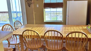 A dining area with a wooden table and chairs, a clock, and a window with blinds. - The Aloha Beach your exquisite property that promises an extraordinary stay! (Surfside Beach)