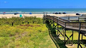A beach with a wooden boardwalk, beach umbrellas, and vehicles. - The Aloha Beach your exquisite property that promises an extraordinary stay! (Surfside Beach)