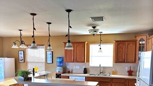 A kitchen with wooden cabinets, a central island with stools, pendant lighting, and a tiled floor. - The Aloha Beach your exquisite property that promises an extraordinary stay! (Surfside Beach)
