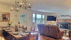 A spacious living room with a large sectional sofa, a fireplace, and a dining area with a long wooden table set for a meal.