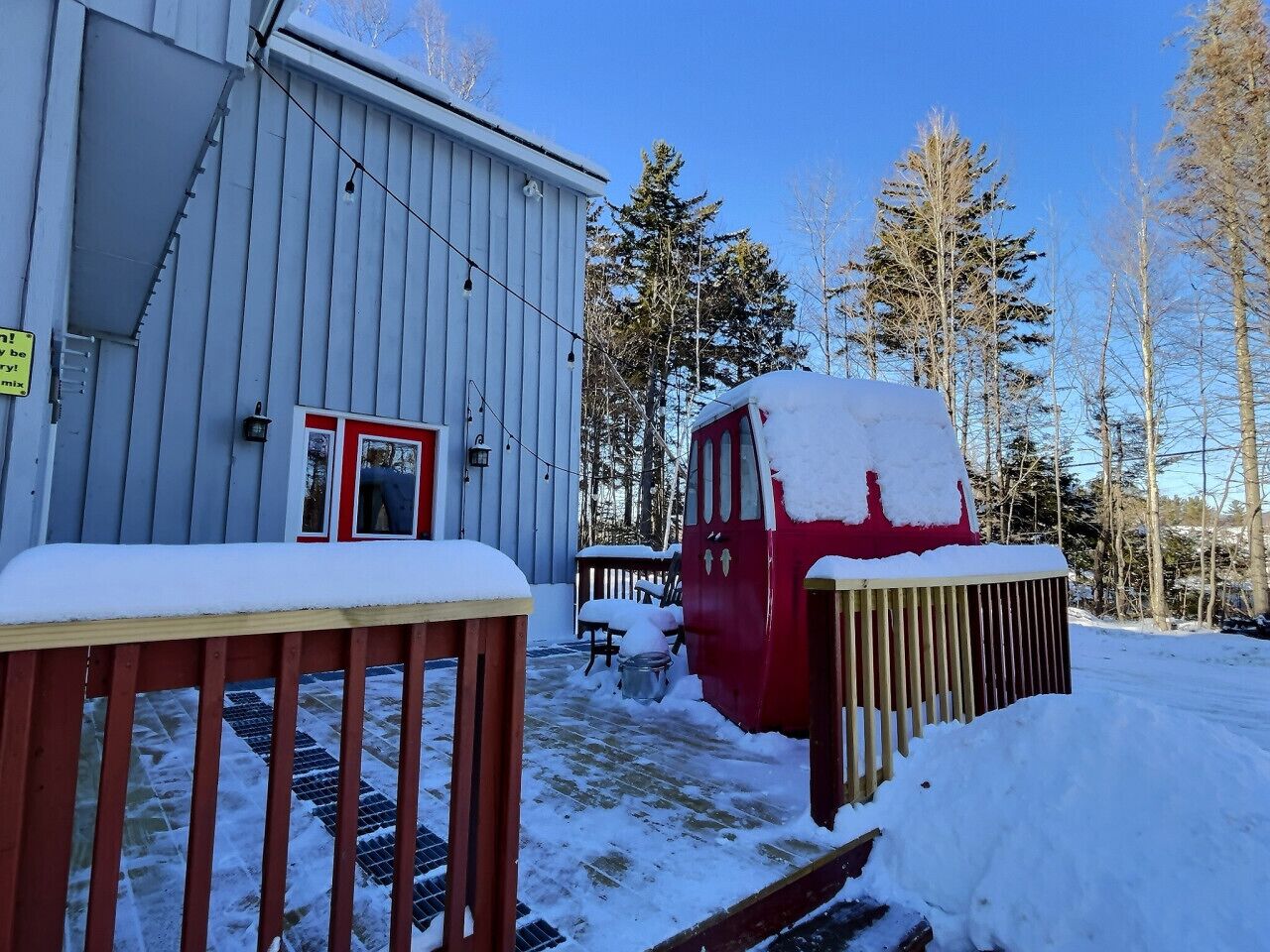 A red vehicle covered in snow parked in front of a building with a red door.