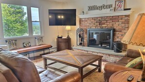 A cozy living room with leather furniture, a fireplace, a TV, and a bench by the window.