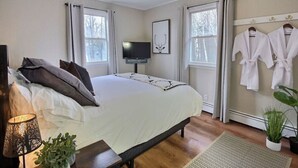 A bedroom with a bed, a TV, a window, and a robe rack.