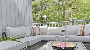 A cozy outdoor seating area with a grey sectional sofa, wicker chairs, and a wooden coffee table. - SugarBear- Pool, AC, Sauna, Gym, Tennis! (Killington)