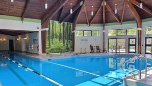 Une piscine intérieure avec des couloirs bien délimités, des poutres en bois et des fenêtres donnant sur un espace verdoyant.
