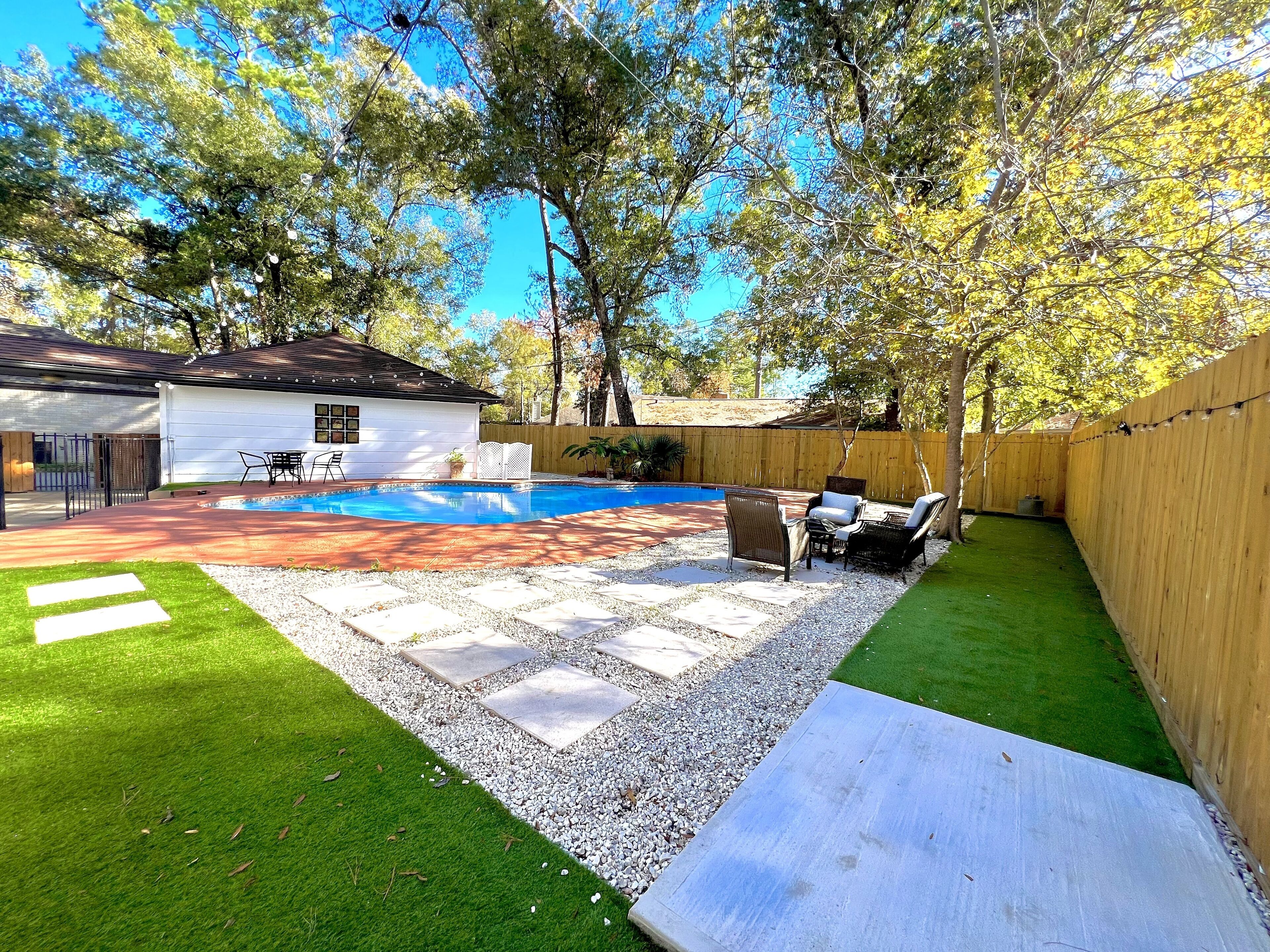 Un patio trasero con piscina, un porche con mobiliario exterior y un pequeño edificio blanco.