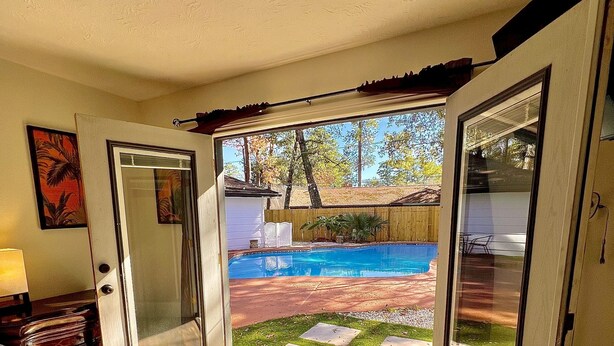 A bedroom with a large sliding glass door leading to a backyard with a swimming pool and a wooden deck.