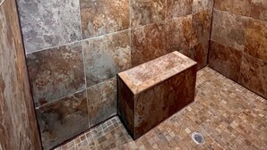 A shower area with large, rectangular tiles and a bench.
