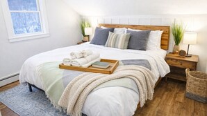 A neatly made bed with a wooden headboard, a bedside table with a lamp, and a window with a view of trees. - BearQuad- AC, Pool, Tennis, Close to Resort/Biking (Killington)