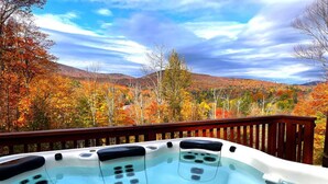 A hot tub with three jets, set on a wooden deck with a scenic view of autumn foliage and hills. - Beartopia- Hot Tub, Views, 2 Primary Suites! (Killington)