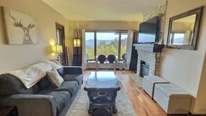 A living room with a fireplace, a sofa, a coffee table, and a view of the outdoors. - Rockstar - Pool, Tennis, Fireplace, Pickleball (Killington)