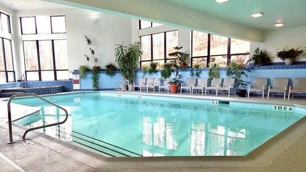 An indoor swimming pool with clear water, surrounded by windows and potted plants. - Rockstar - Pool, Tennis, Fireplace, Pickleball (Killington)