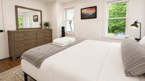 A bedroom with a bed, a dresser, a mirror, a window with a view of greenery, and a lamp. - CubsCorner - Pool, Sauna, Gym, Close to Mountain! (Killington)