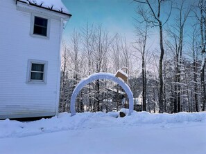 A white building with two windows, surrounded by snow-covered trees and a metal sculpture in the foreground. - CubsCorner - Pool, Sauna, Gym, Close to Mountain! (Killington)