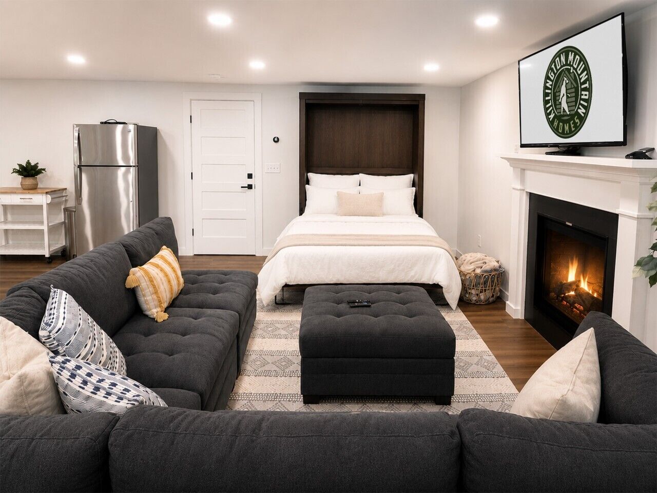 A modern bedroom with a bed, a sofa, a fireplace, and a television.