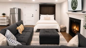 A modern bedroom with a bed, a sofa, a fireplace, and a television.