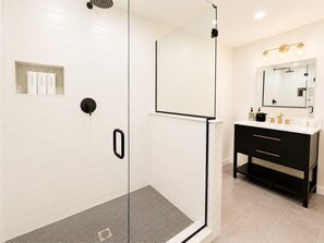 A modern bathroom with a glass-enclosed shower, a vanity with a mirror, and a tiled floor. - CubsCorner - Pool, Sauna, Gym, Close to Mountain! (Killington)