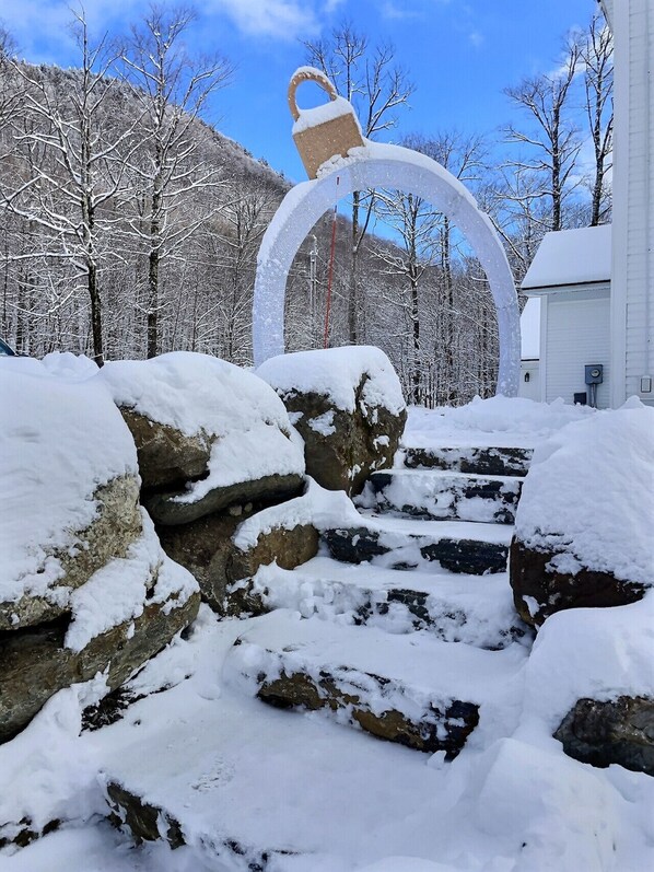 A snow-covered outdoor area with a large arch structure, rocks, and a building in the background. - CubsCorner - Pool, Sauna, Gym, Close to Mountain! (Killington)