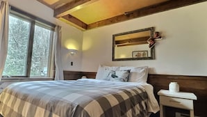 A bedroom with a large bed, a nightstand, a mirror, and a window with curtains.
