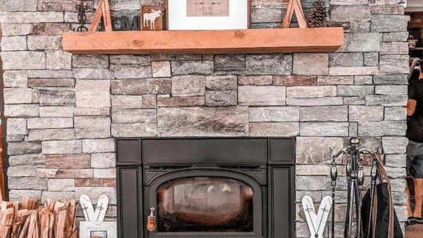 A stone fireplace with a black mantel, framed picture, and decorative items.