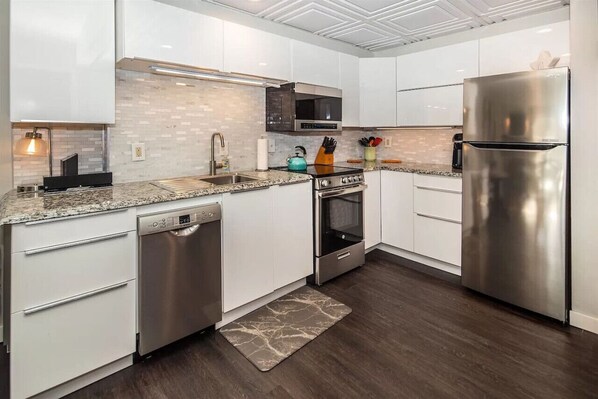 A modern kitchen with white cabinets, stainless steel appliances, and a granite countertop.