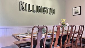 A dining area with a wooden table and chairs, a wall-mounted sign reading "KILLINGTON", and a framed picture on the wall. - DoubleDen Lower- AC, Fire place, Game Room (Killington)