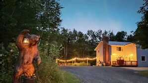 A rustic cabin with a bear statue in front, surrounded by trees and string lights. - DoubleDen Lower- AC, Fire place, Game Room (Killington)