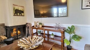 A living room with a fireplace, a wooden table, and a television mounted on the wall. - DoubleDen Lower- AC, Fire place, Game Room (Killington)