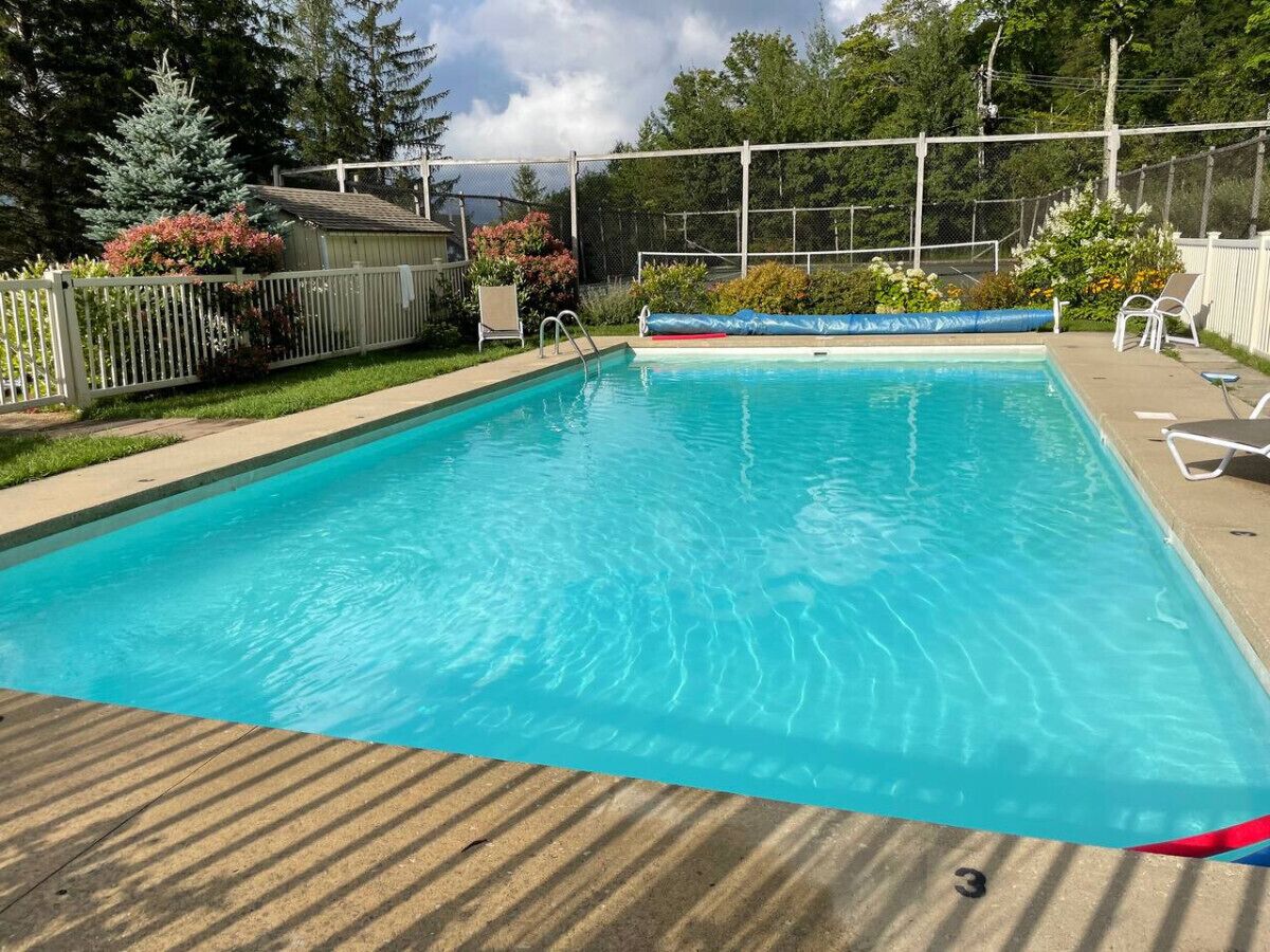 A rectangular swimming pool with clear blue water, surrounded by a wooden deck and a white fence.
