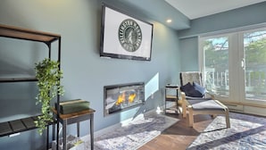 A modern living room with a fireplace, a framed clock, and a large window. - Moose Tracks Lodge - Pool, Hot Tub, Golf, Sauna (Killington)