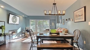 A dining area with a wooden table and chairs, a chandelier, and a view of the outdoors through large windows. - Moose Tracks Lodge - Pool, Hot Tub, Golf, Sauna (Killington)