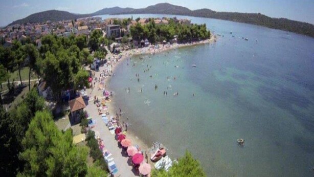 A coastal town with a beach, clear water, and a row of beach umbrellas.
