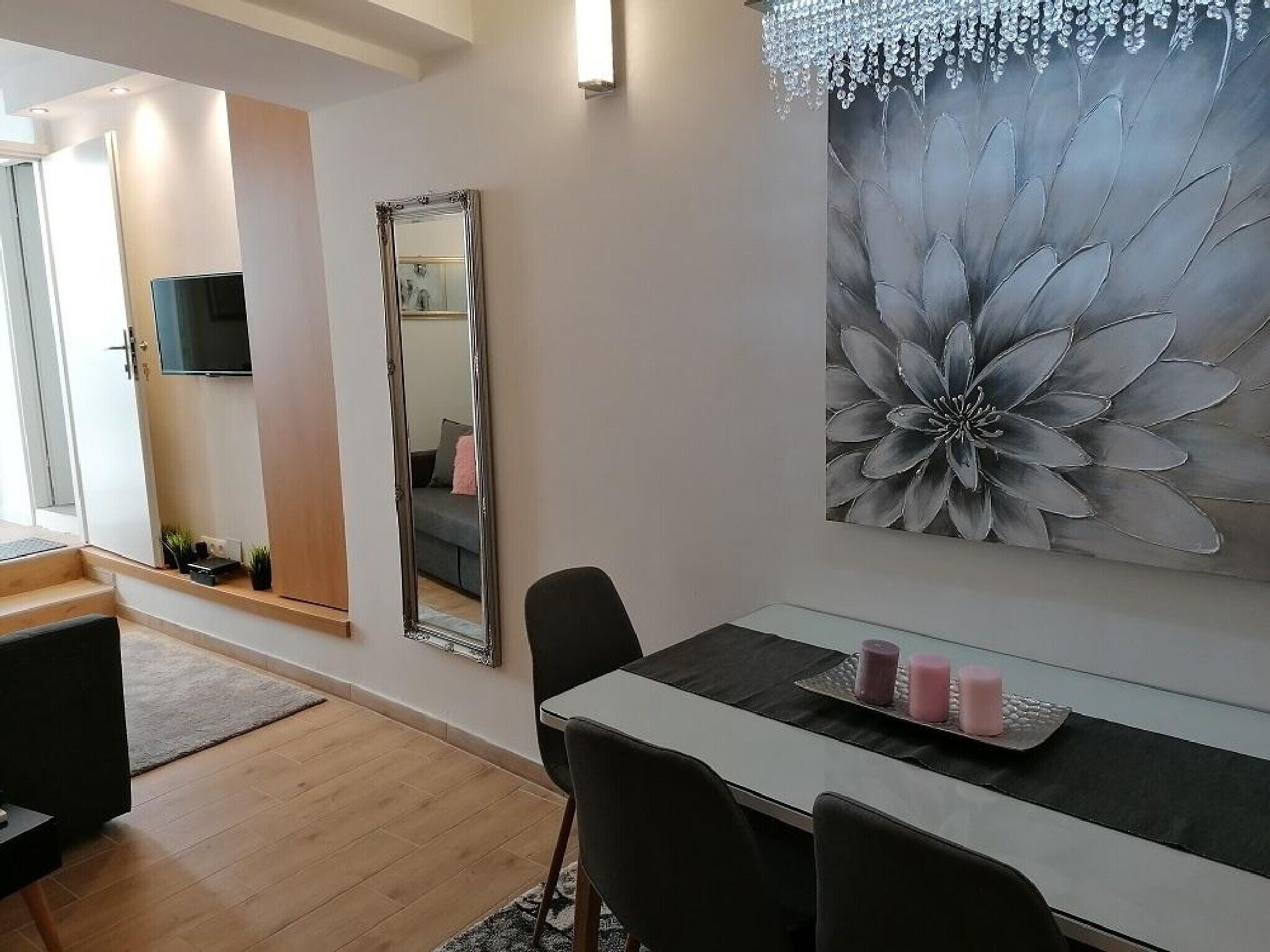 A modern living room with a dining area, a large mirror, and a floral artwork on the wall.