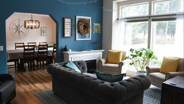 A living room with a dark-colored sofa, a fireplace, and a dining area with a table and chairs. - Large Kitchen, Hot tub, Game & Arcade Room (Hayden)