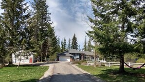 A rural driveway leading to a house with a garage, surrounded by trees and a white fence. - Large Kitchen, Hot tub, Game & Arcade Room (Hayden)