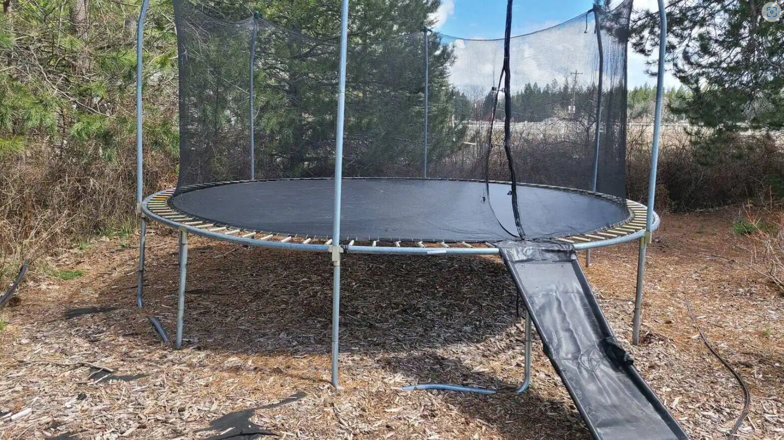 Un trampoline doté d’un filet de protection, entouré d’arbres et de paillis.