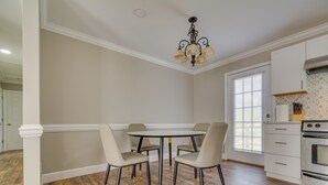A dining area with a round table and four chairs, a chandelier, and a kitchen with white cabinets and a stove. - Bailey Vacation Rental, 13 Mi to Downtown Wilson (Bailey)