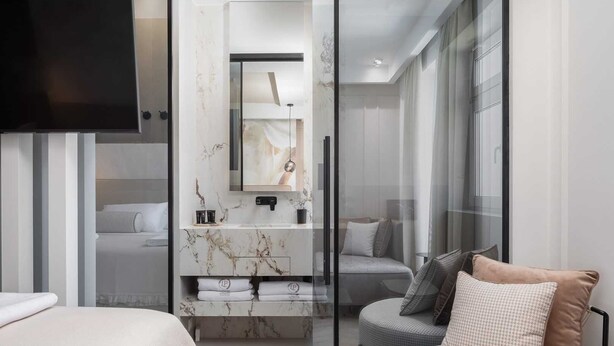 Et moderne hotelværelse med en stor seng, et opholdsområde med puder, et sminkebord med spejl og et fjernsyn.