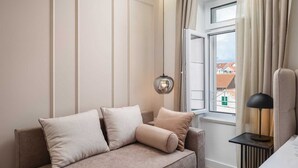 Ein modernes Hotelzimmer mit einem beigen Sofa, einem Beistelltisch mit Lampe und einem Fenster mit Vorhängen.