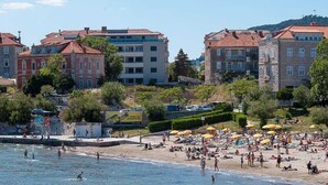 Platja amb gent prenent el sol i banyant-se, envoltada d'edificis amb teulades vermelles.