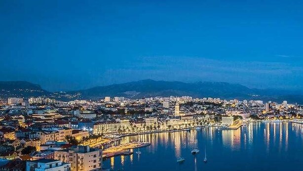 A coastal cityscape at dusk with a prominent waterfront promenade, a marina, and a distant mountain range. - Elegance Room in Split (Split)