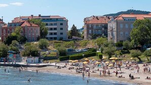 A beach with people sunbathing and swimming, surrounded by buildings with red-tiled roofs. - Elegance Room in Split (Split)
