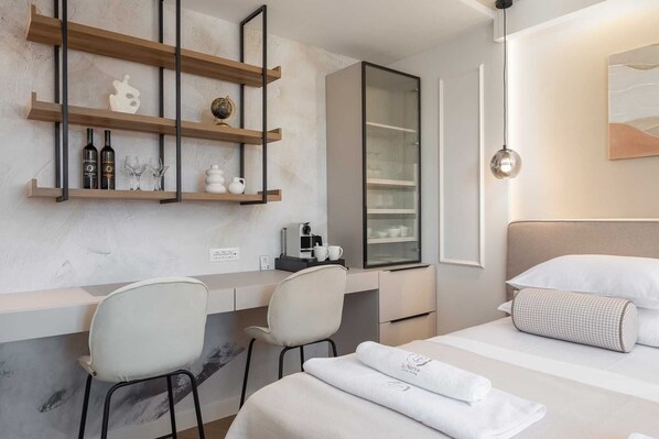 Ein modernes Hotelzimmer mit einem Bett, einem Schreibtisch mit Stühlen, einer Kaffeemaschine und einer Minibar.